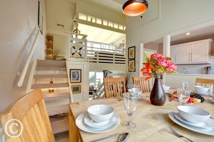 Dining area with view of the kitchen, open tread stairs lead to additional seating area with TV. View of the kitchen from the dining area, stairs upto additional seating area